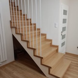 Zakład stolarski Mroczek - Drewniane schody z białymi, pionowymi balustradami w nowoczesnym wnętrzu, widok z dołu na pierwsze stopnie i część biegu schodów.