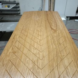 Zakład stolarski Mroczek - Jasny, drewniany blat z wyfrezowanym wzorem w jodełkę, widoczny w warsztacie stolarskim.