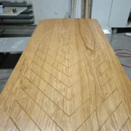 Jasny, drewniany blat z wyfrezowanym wzorem w jodełkę, widoczny w warsztacie stolarskim.