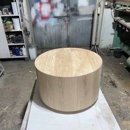 Zakład stolarski Mroczek - Okrągły blat drewniany o jasnym odcieniu w warsztacie stolarskim, widoczne drzwi warsztatu i regał z farbami