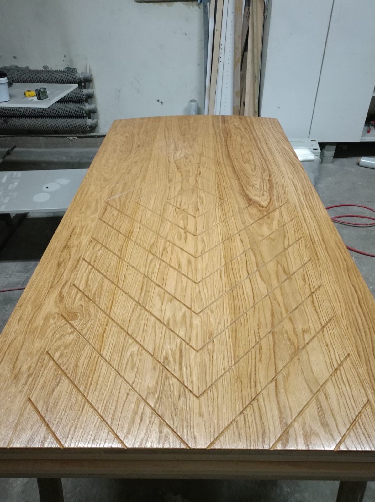 Jasny, drewniany blat z wyfrezowanym wzorem w jodełkę, widoczny w warsztacie stolarskim.