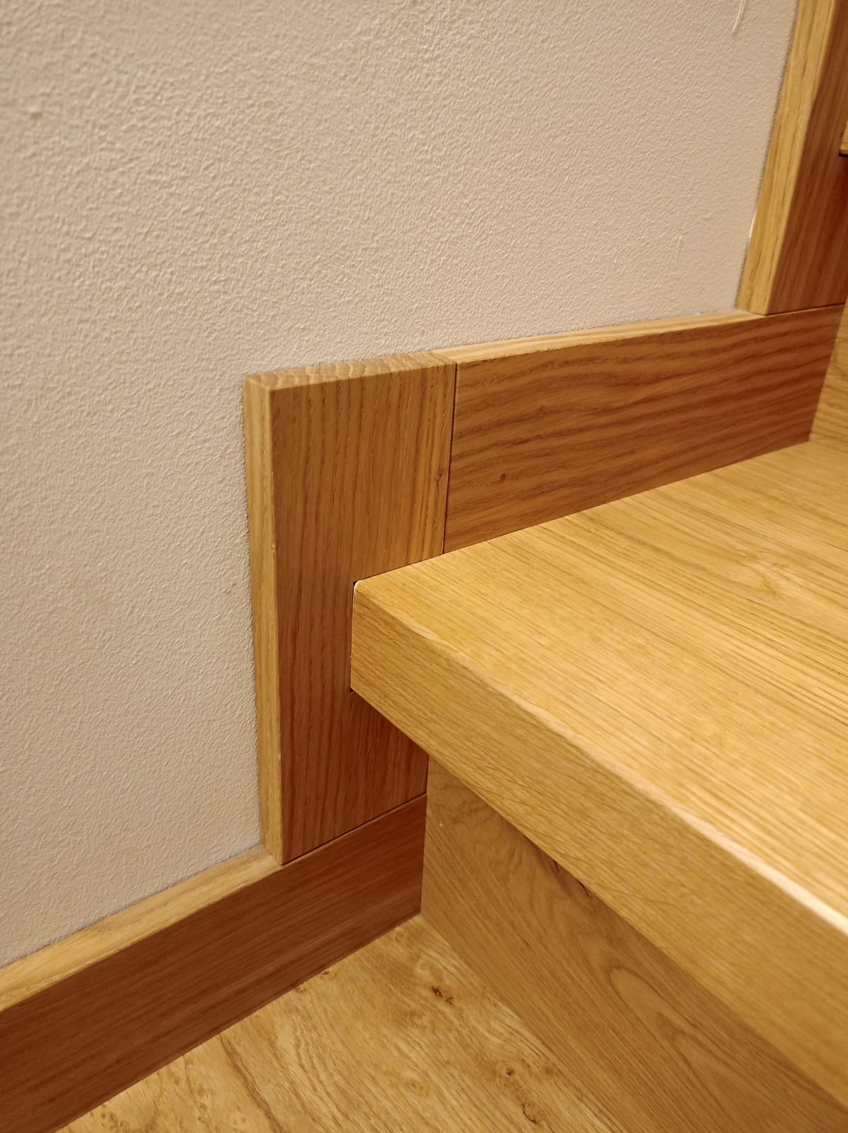 Detale wykończenia wnętrza: drewniane listwy przypodłogowe z dębowym fornirem, dopasowane do schodów, przy ścianie z delikatną fakturą.