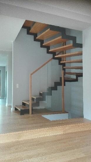 Nowoczesne, ażurowe schody drewniane z czarnymi elementami konstrukcyjnymi i jasną balustradą w domu w Kłecku, widok z dołu na tle jasnych ścian i podłogi.