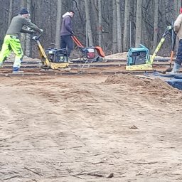 OM-GOR OLEH HORBYK - Prace ziemne w trakcie wyrównywania terenu pod budowę, pracownicy używają zagęszczarek w pobliżu lasu.