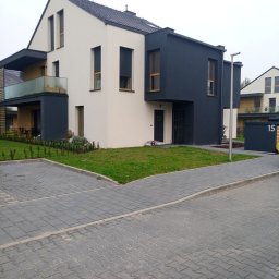 OM-GOR OLEH HORBYK - Nowoczesny dom dwukondygnacyjny z płaskim dachem, elewacja w kolorze bieli i antracytu, z oknami z drewnianą ramą, otoczony trawnikiem i brukowanym podjazdem.