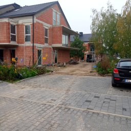 OM-GOR OLEH HORBYK - Budowa bliźniaka z czerwonej cegły, widoczne niezadaszone okna, teren budowy z ogrodzeniem i zaparkowany samochód w tle.