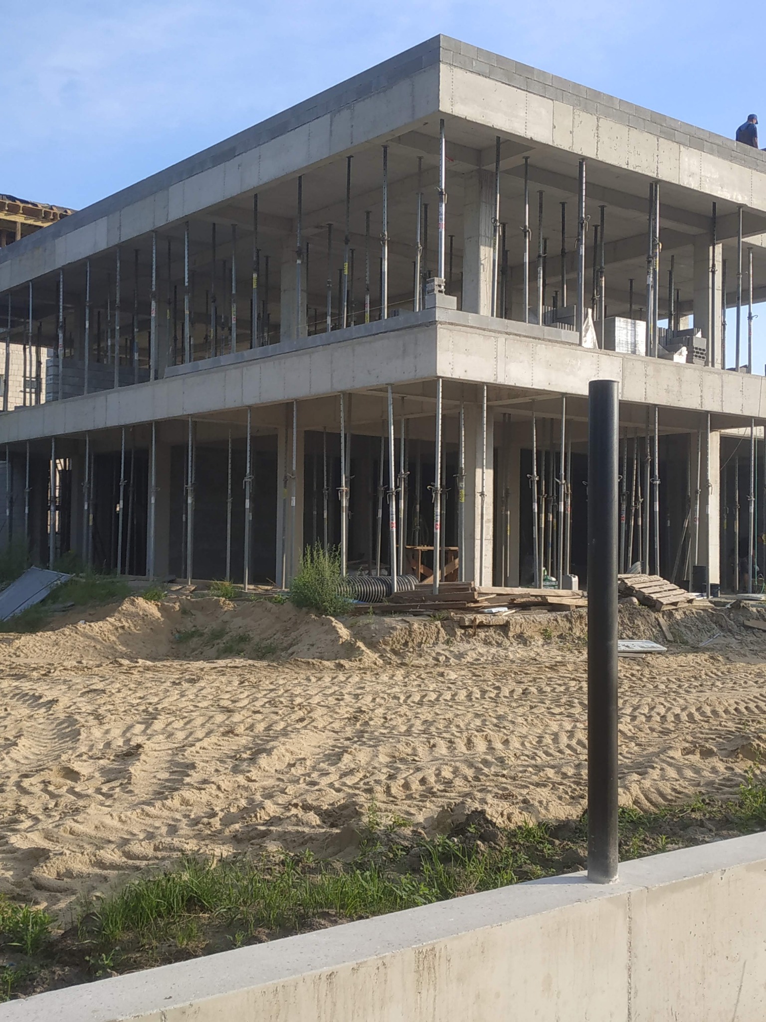 Surowy stan budynku żelbetowego w Skierniewicach, widoczne podpory szalunkowe i zbrojenie, teren wokół w stanie przygotowania.
