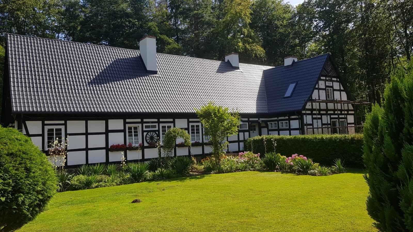 Dom w stylu szachulcowym z nowym, ciemnoszarym dachem z dachówki ceramicznej, widok z zadbanego ogrodu.