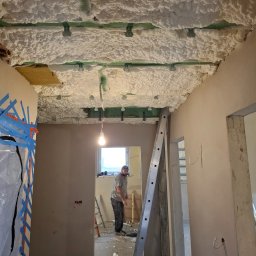 A.P. SOLID ANDRZEJ PAWLAK - Ocieplenie pianą PUR stropu w trakcie remontu, widoczne profile mocujące, drabina oparta o ścianę, pracownik w tle przy oknie.