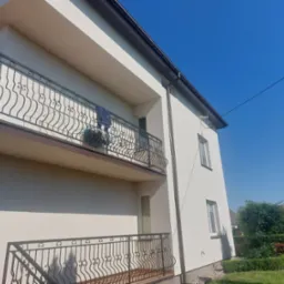 Elewacja dwupiętrowego domu z balkonami z kutą balustradą, świeżo po remoncie, w słoneczny dzień.