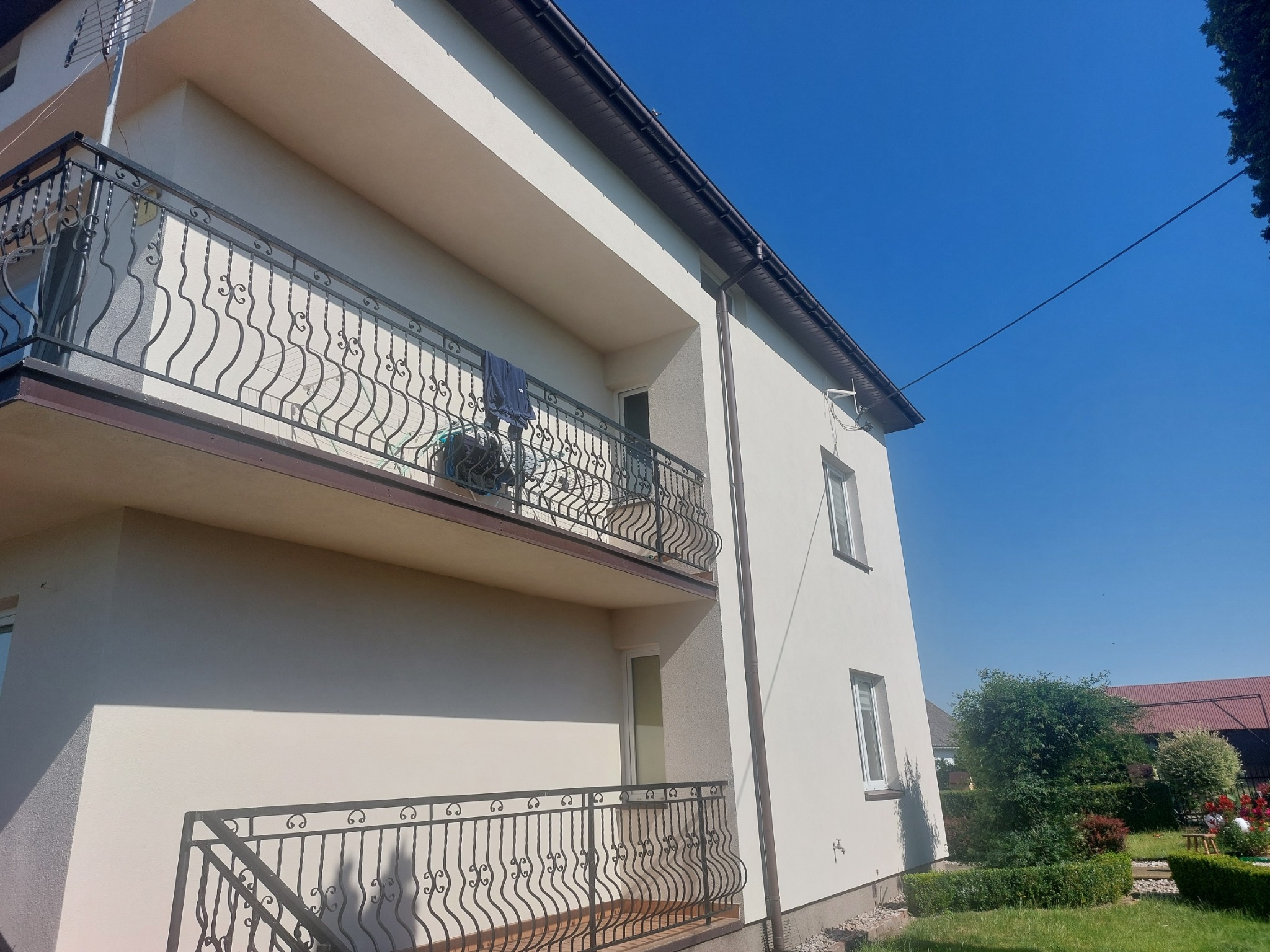 Elewacja dwupiętrowego domu z balkonami z kutą balustradą, świeżo po remoncie, w słoneczny dzień.