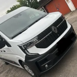 Nowoczesny, biały bus Renault z czarnymi akcentami, zaparkowany na zewnątrz. Ujęcie z niskiego kąta podkreśla detale przedniej części pojazdu.