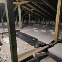 Izolacja poddasza pianką EPS, widoczne krokwie, rury wentylacyjne i instalacja elektryczna w trakcie montażu.