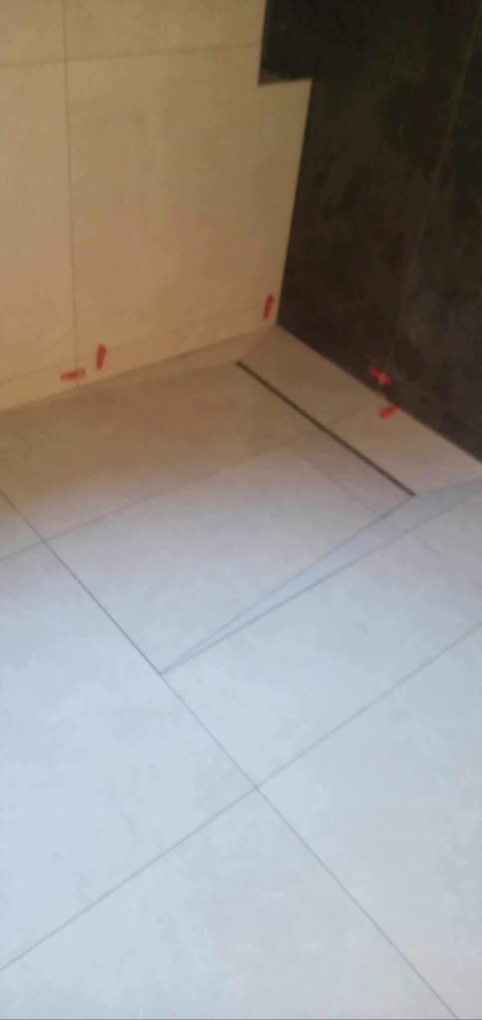 Ułożone jasne płytki podłogowe z krzyżykami dystansowymi, fragment ściany wykończonej beżowymi i ciemnymi płytkami.