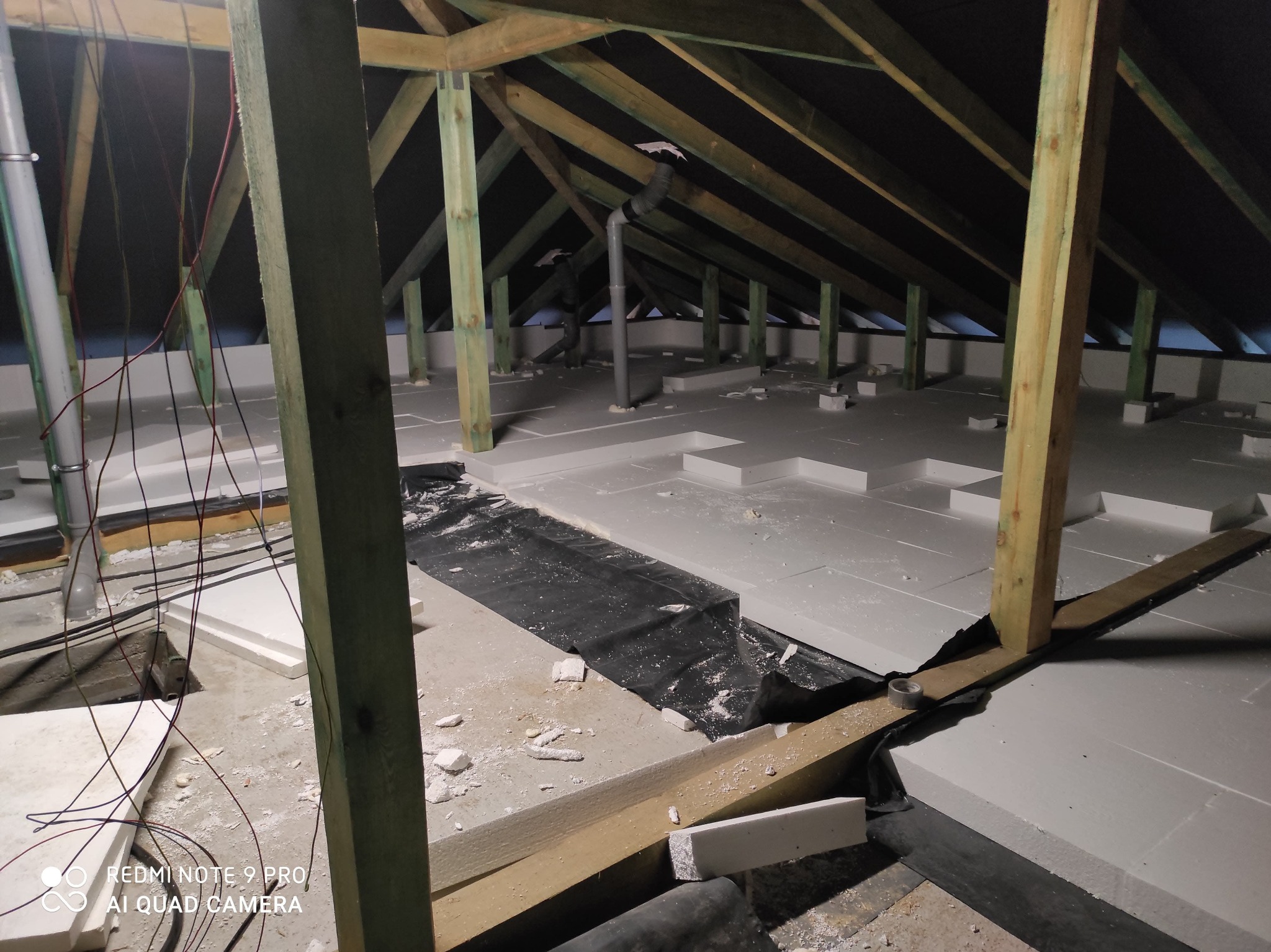 Izolacja poddasza pianką EPS, widoczne krokwie, rury wentylacyjne i instalacja elektryczna w trakcie montażu.