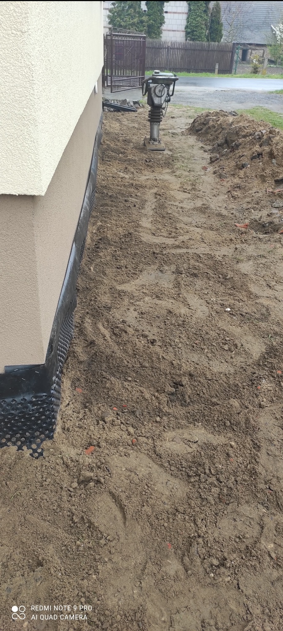 Ocieplenie fundamentu budynku z użyciem folii kubełkowej, ubijarka gruntu w tle.