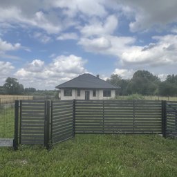 Twoje Ogrodzenie 24 - Nowoczesne, poziome, ciemnoszare przęsła ogrodzeniowe z widokiem na dom w tle, na tle błękitnego nieba z obłokami.