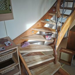 Łukasz Gałka Złota Rączka - Drewniane schody z metalową balustradą w kształcie gałęzi, puszka z bejcą i pędzel na stopniu, widoczne materiały ścierne i ściereczka, etap renowacji schodów.