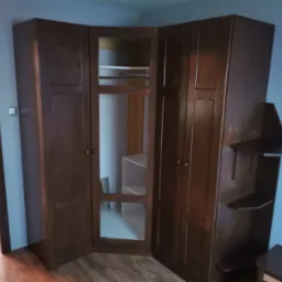 Kątowa szafa wnękowa z ciemnego drewna z przeszklonymi drzwiami, widoczne półki wewnątrz, dodatkowe półki boczne, montaż w pokoju z niebieską ścianą.