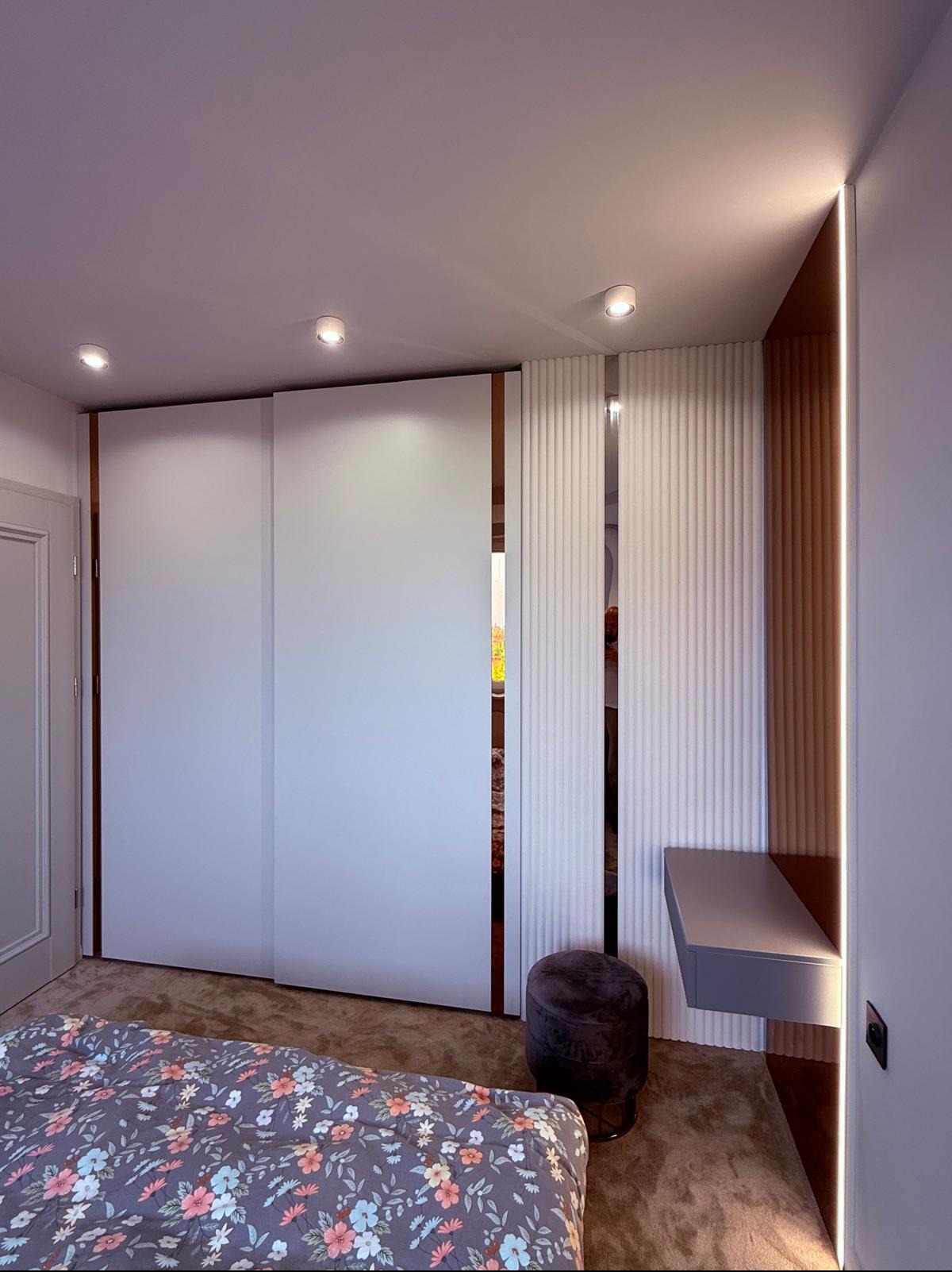 Nowoczesna szafa przesuwna z białymi frontami i dekoracyjnymi panelami ściennymi w sypialni. Realizacja z Wyszogrodu z subtelnym oświetleniem LED.