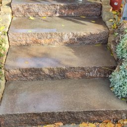 YOKO-BUD - Granitowe schody zewnętrzne z brązowo-szarego kamienia, pokryte opadłymi żółtymi liśćmi, prowadzące do jasnej kostki brukowej.