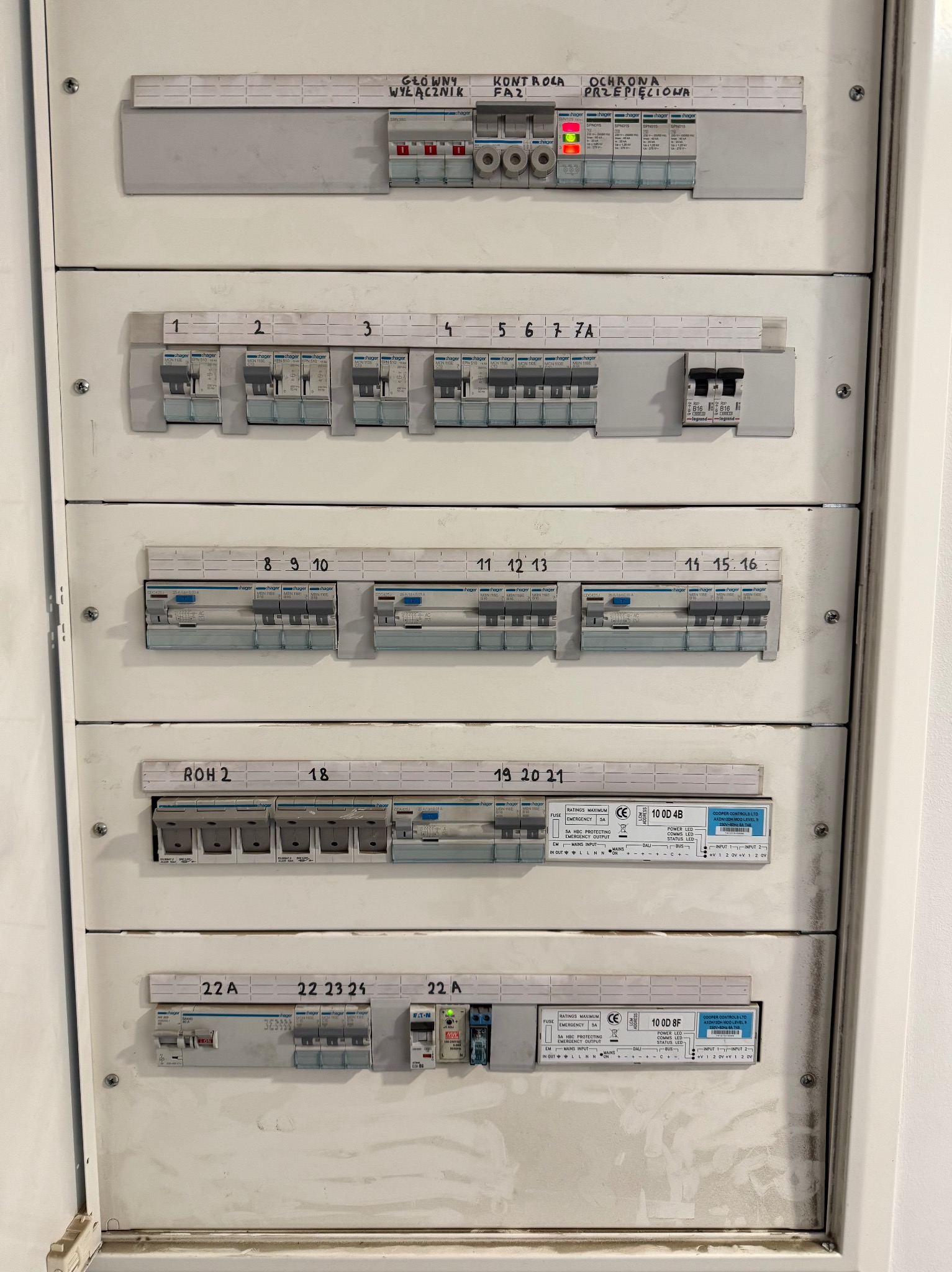 Rozdzielnica elektryczna z bezpiecznikami i wyłącznikami, widoczne oznaczenia numerów i parametrów. Element instalacji elektrycznej wewnątrz budynku.