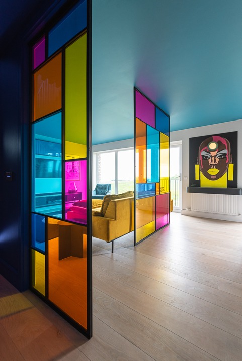 Kolorowa szklana ścianka działowa w salonie z żółtą sofą i obrazem na ścianie, jasna podłoga, błękitny sufit. Nowoczesny design wnętrza.