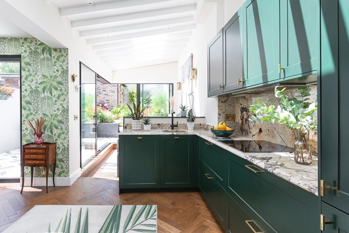 Nowoczesna kuchnia z zielonymi szafkami i drewnianą podłogą w jodełkę, z widokiem na taras przez przeszklone drzwi.