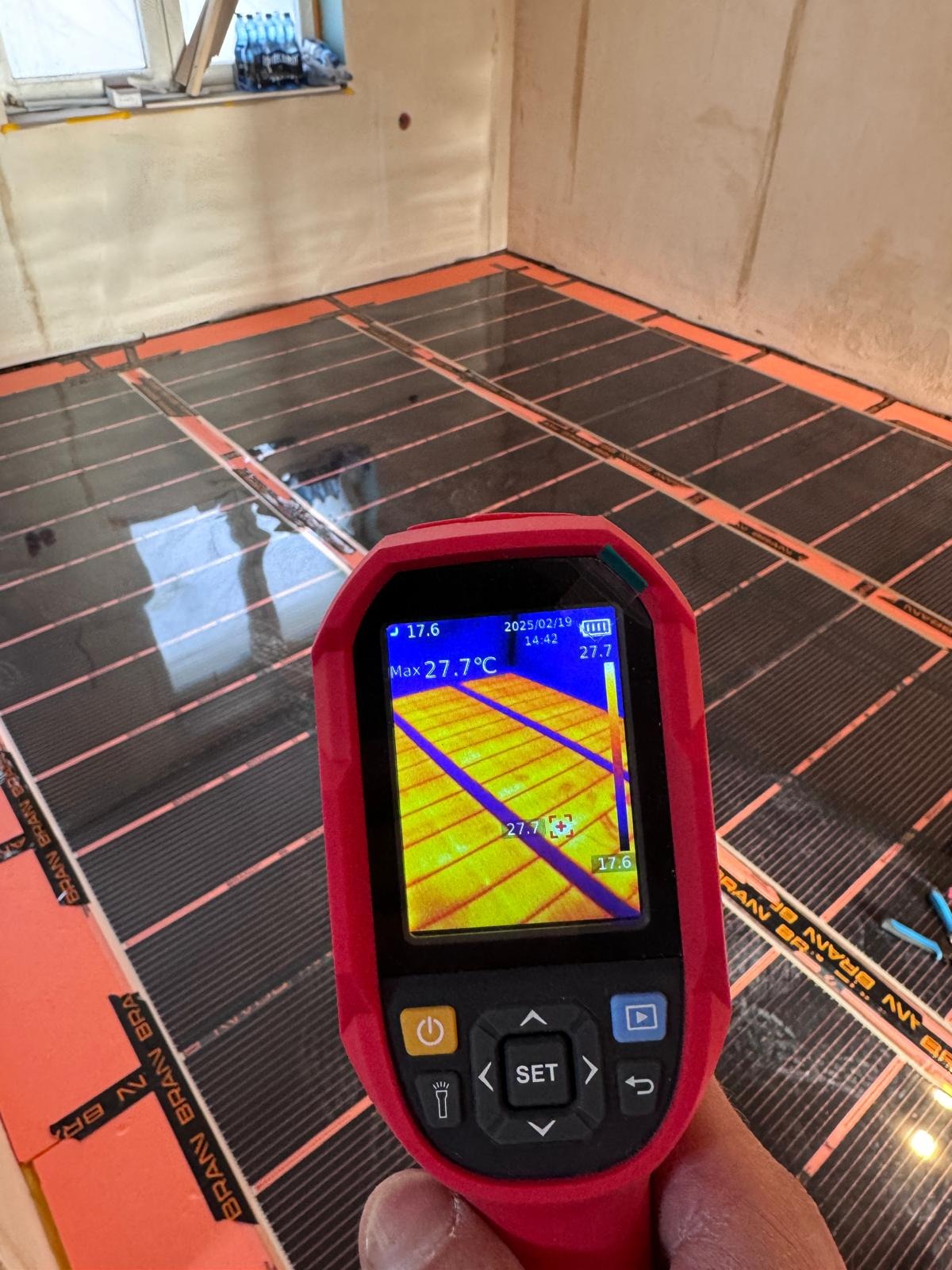 Pomiar temperatury podłogowego ogrzewania elektrycznego za pomocą kamery termowizyjnej; widoczny rozkład temperatur na ekranie urządzenia.