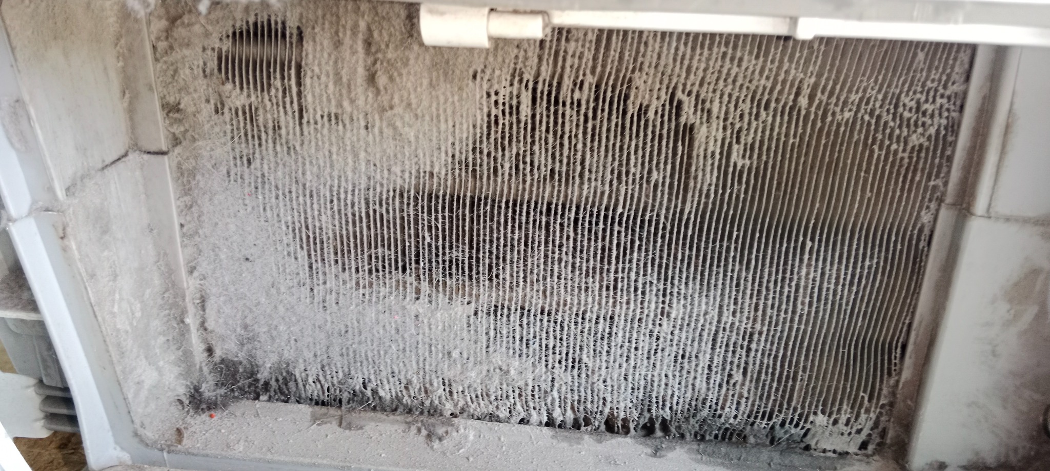 Zanieczyszczony, zakurzony filtr urządzenia, prawdopodobnie klimatyzacji lub wentylacji, z widocznymi nagromadzeniami kurzu i brudu na lamelach i obudowie.