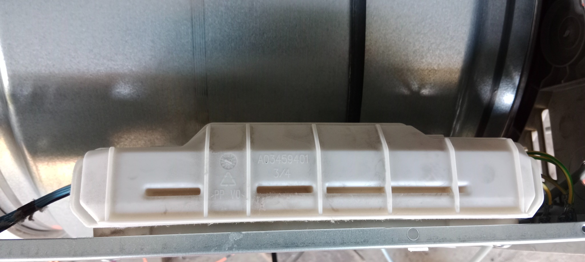 Wnętrze urządzenia AGD z widocznym, białym elementem z tworzywa sztucznego oznaczonym numerem A03459401 i widocznymi przewodami elektrycznymi.