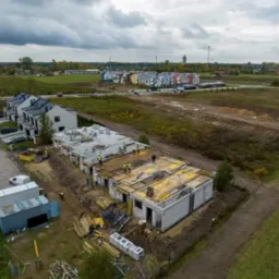 Budowa szeregu domów jednorodzinnych z betonu komórkowego, widok z lotu ptaka, z widocznymi pracownikami w żółtych kamizelkach, drewnianym szalunkiem i przygotowanym terenem pod kolejne etapy...