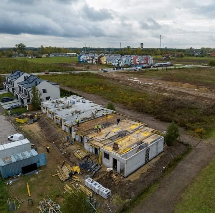 Budowa szeregu domów jednorodzinnych z betonu komórkowego, widok z lotu ptaka, z widocznymi pracownikami w żółtych kamizelkach, drewnianym szalunkiem i przygotowanym terenem pod kolejne etapy...