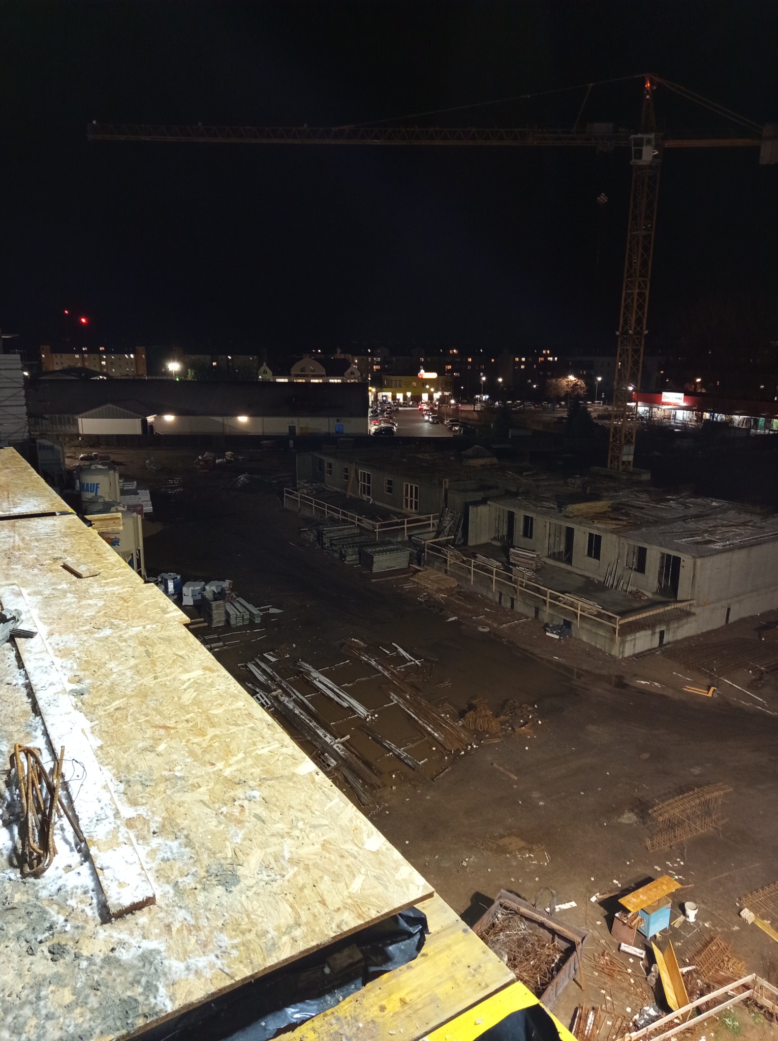 Nocny widok z góry na plac budowy z częściowo wzniesionymi budynkami z betonu komórkowego, widoczny dźwig budowlany na tle miejskiego oświetlenia.