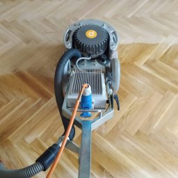 EXOWOOD Kamil Olechowski - Maszyna do cyklinowania w trakcie pracy na parkiecie ułożonym w jodełkę, widoczne różnice w kolorze drewna po cyklinowaniu.