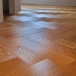 Ułożony parkiet w jodełkę w jasnym pomieszczeniu z oknem dachowym, widoczne niedokończone wykończenia ścian.