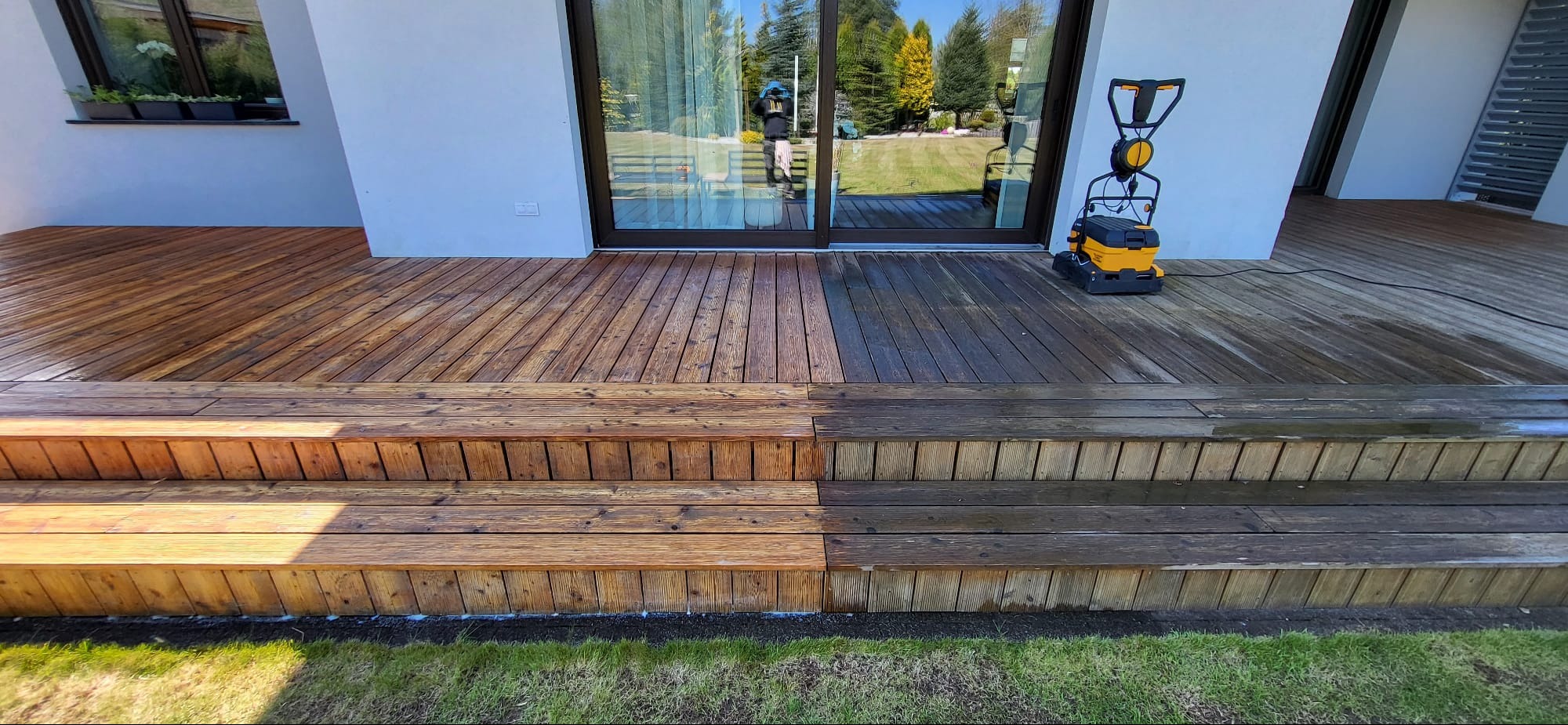 Czyszczenie drewnianego tarasu schodkowego z użyciem myjki ciśnieniowej; widoczna różnica między wyczyszczoną a nieczyszczoną częścią tarasu.