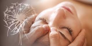 Kobieta z zamkniętymi oczami poddawana delikatnemu masażowi twarzy, z nałożonym graficznie motywem dmuchawca, sugerującym lekkość i ulgę.