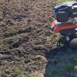 Ogród Dom - Przygotowana gleba pod uprawę, świeżo przekopana glebogryzarką marki Stihl, widoczne resztki trawy i korzeni, w tle żywopłot.