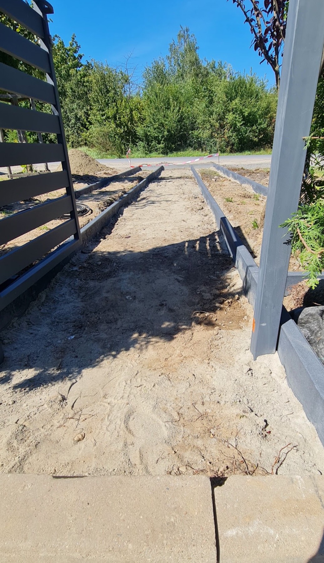 Przygotowanie podłoża pod ścieżkę w ogrodzie w Gorzowie Wielkopolskim, widoczne obrzeża i piasek, brama w tle.