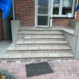 Mirosław Nieśpiał Mr Handy - Wyłożone płytkami schody wejściowe do domu z cegły, widoczne białe krzyżyki dystansowe między płytkami na stopniach i częściowo uszkodzona kostka brukowa przed schodami.