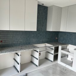 Mirosław Nieśpiał Mr Handy - Montaż białych szafek kuchennych z szarym blatem i niebieską mozaiką w tle, widoczne szyny do szuflad, instalacja w Józefowie w trakcie realizacji.