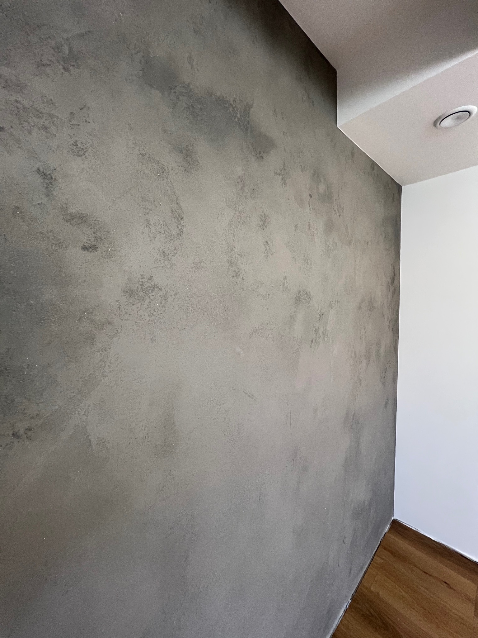 Ściana z efektem dekoracyjnym w odcieniach szarości, wykonana w Józefowie, z widocznym fragmentem białego sufitu i podłogi z paneli.