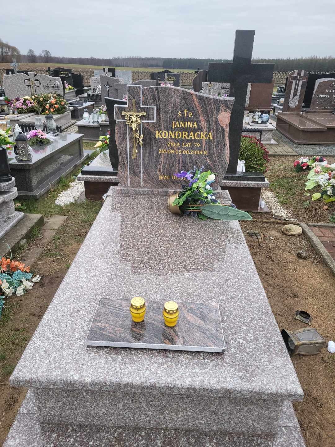 Granitowy nagrobek z wyrytym imieniem i nazwiskiem Janina Kondracka, datą urodzenia i śmierci, ozdobiony krzyżem z Jezusem i kwiatami, z dwoma zapalonymi zniczami na płycie, na cmentarzu z innymi...