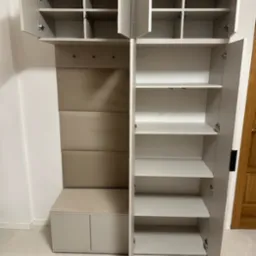 Szara zabudowa przedpokoju z otwartymi szafkami górnymi i dolnymi, siedziskiem z tapicerowanym panelem i wieszakami.