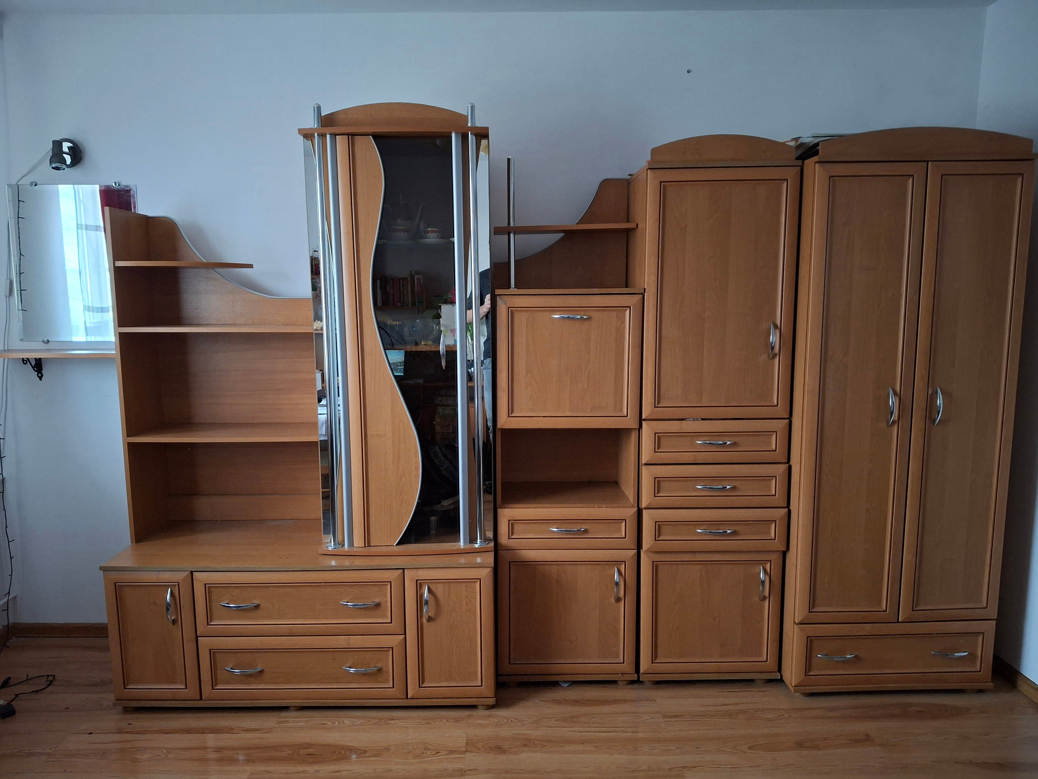 Zestaw mebli pokojowych w odcieniach brązu, składający się z witryny z przeszkleniami, szafek, szuflad i półek, ustawiony na parkiecie.