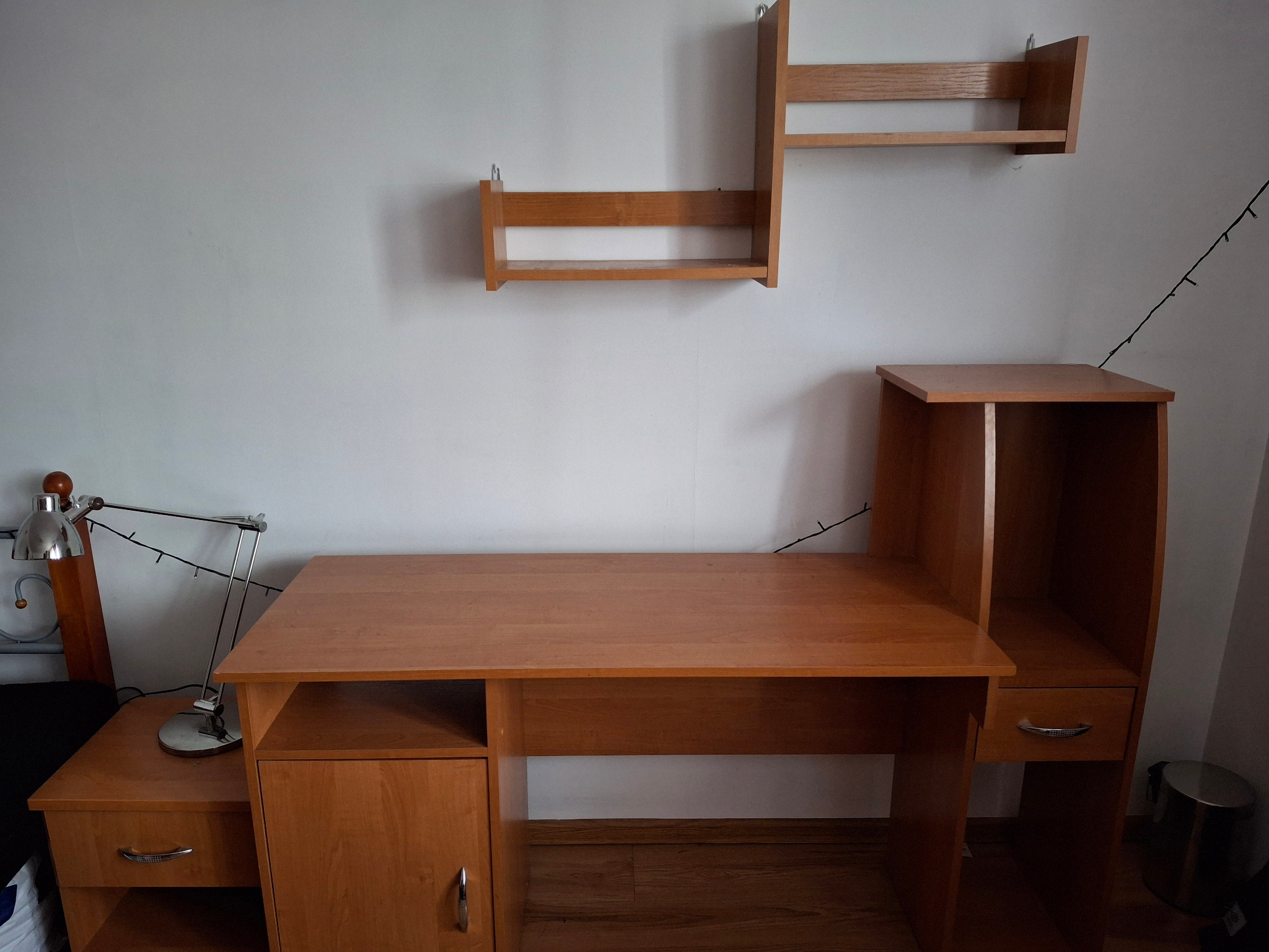 Biurko z nadstawką i półkami w kolorze drewna, zamontowane w pokoju w Osiecku. Widoczna lampka biurkowa i dekoracyjne lampki choinkowe.