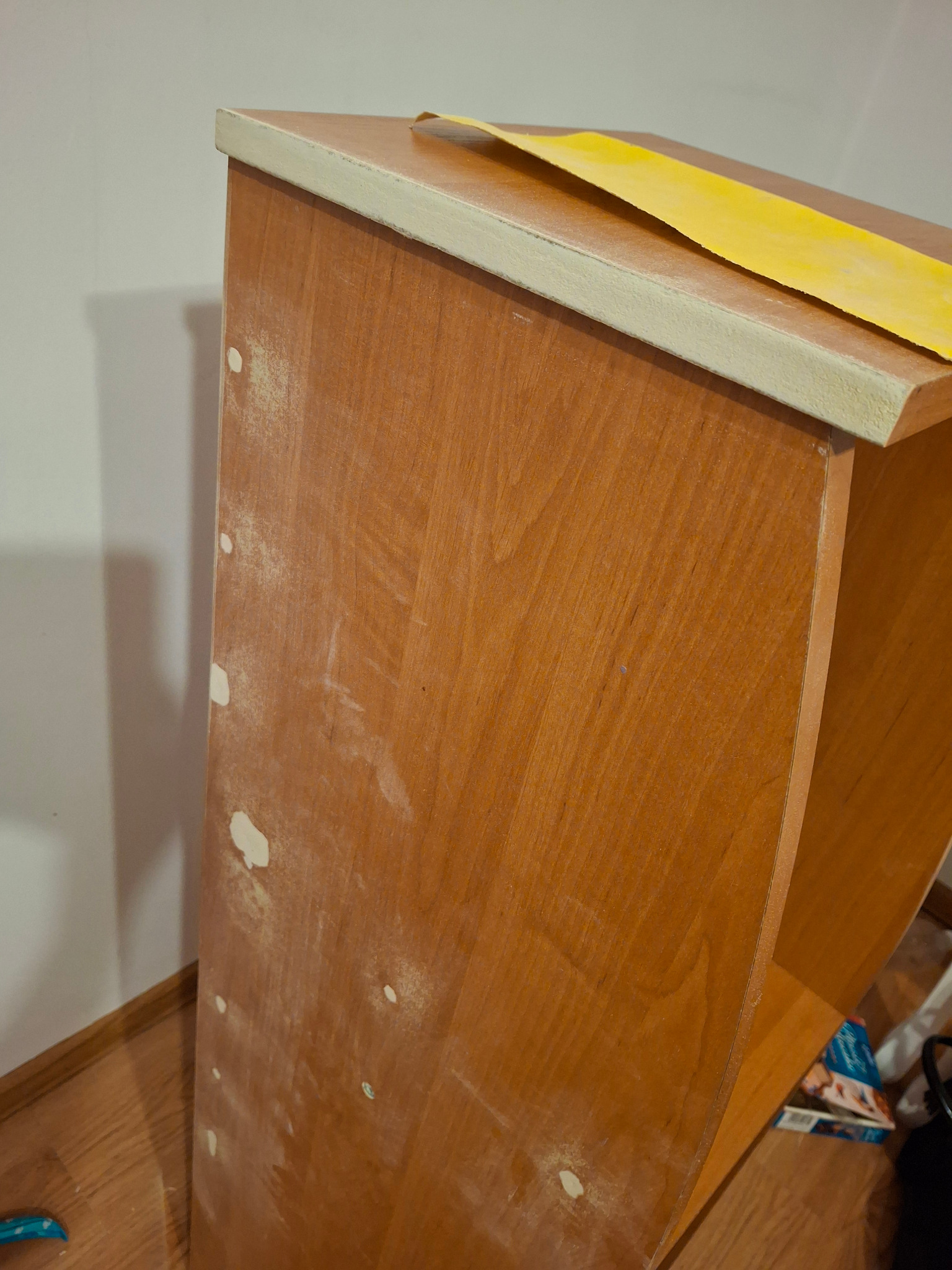 Przygotowanie drewnianej szafki do malowania: szpachlowanie i szlifowanie, widoczne ślady szpachli i żółta taśma malarska zabezpieczająca krawędzie.