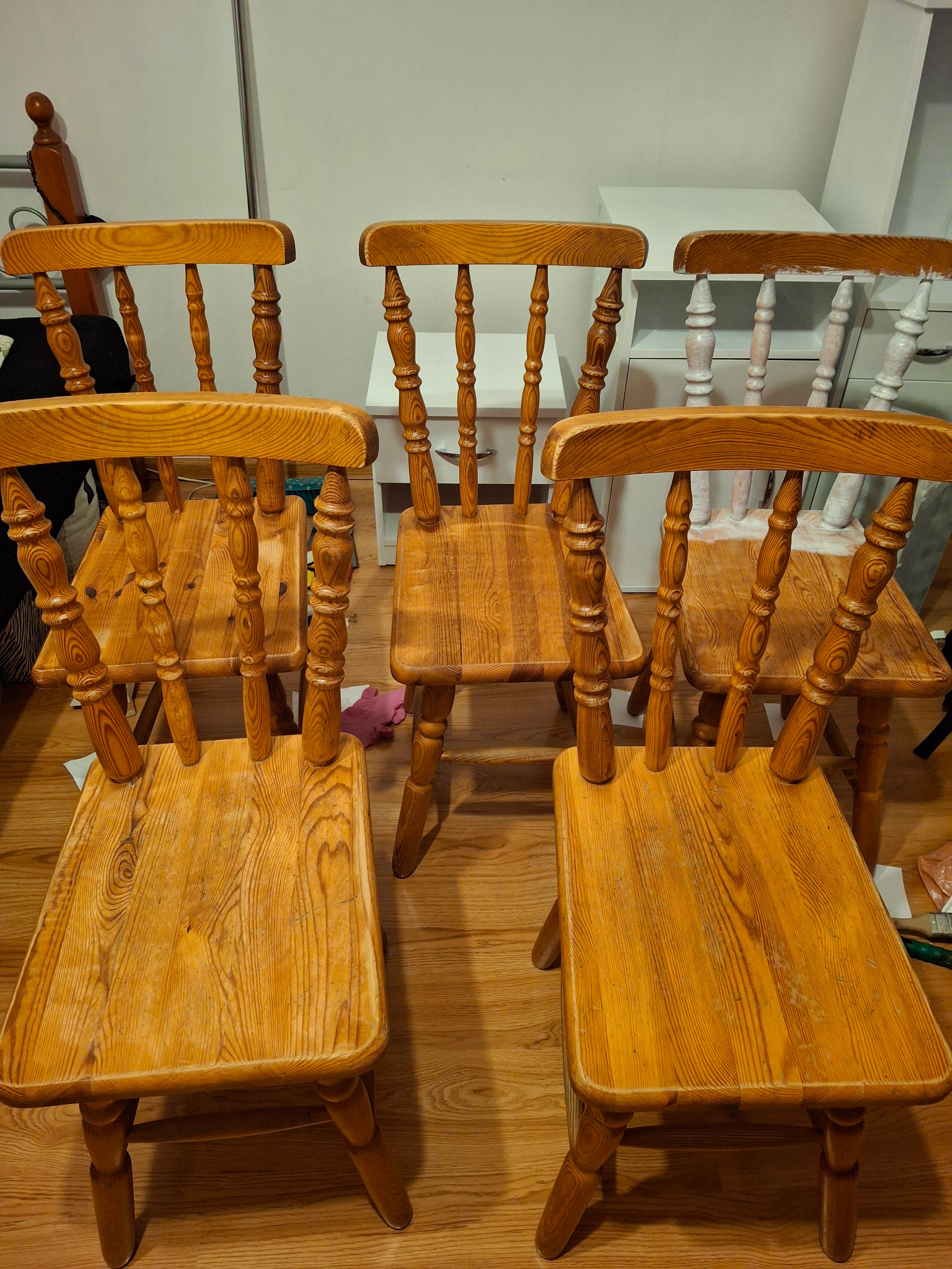 Rząd drewnianych krzeseł typu Windsor w odcieniach miodowego brązu, z widocznymi śladami użytkowania i patyną, ustawionych na drewnianej podłodze w pomieszczeniu o jasnych ścianach.