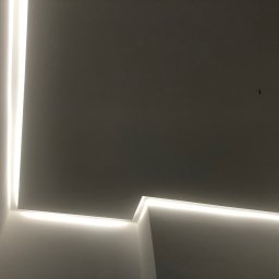 Roman Piddubnyi - Nowoczesne oświetlenie sufitowe LED w narożniku pomieszczenia, tworzące minimalistyczny design z wyraźną linią światła.